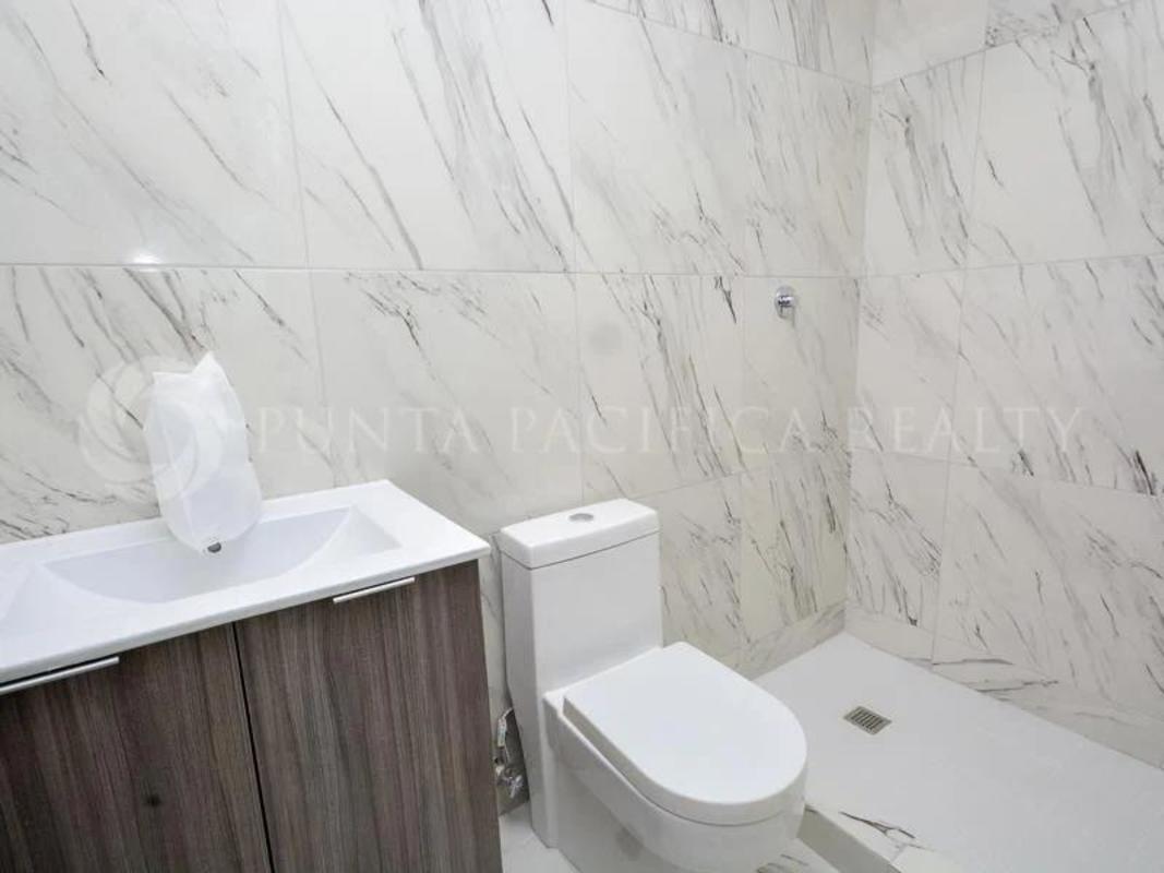 Bathroom with marble wall tiles, glass shower enclosure, and wood vanity in PH El Botánico Panama City