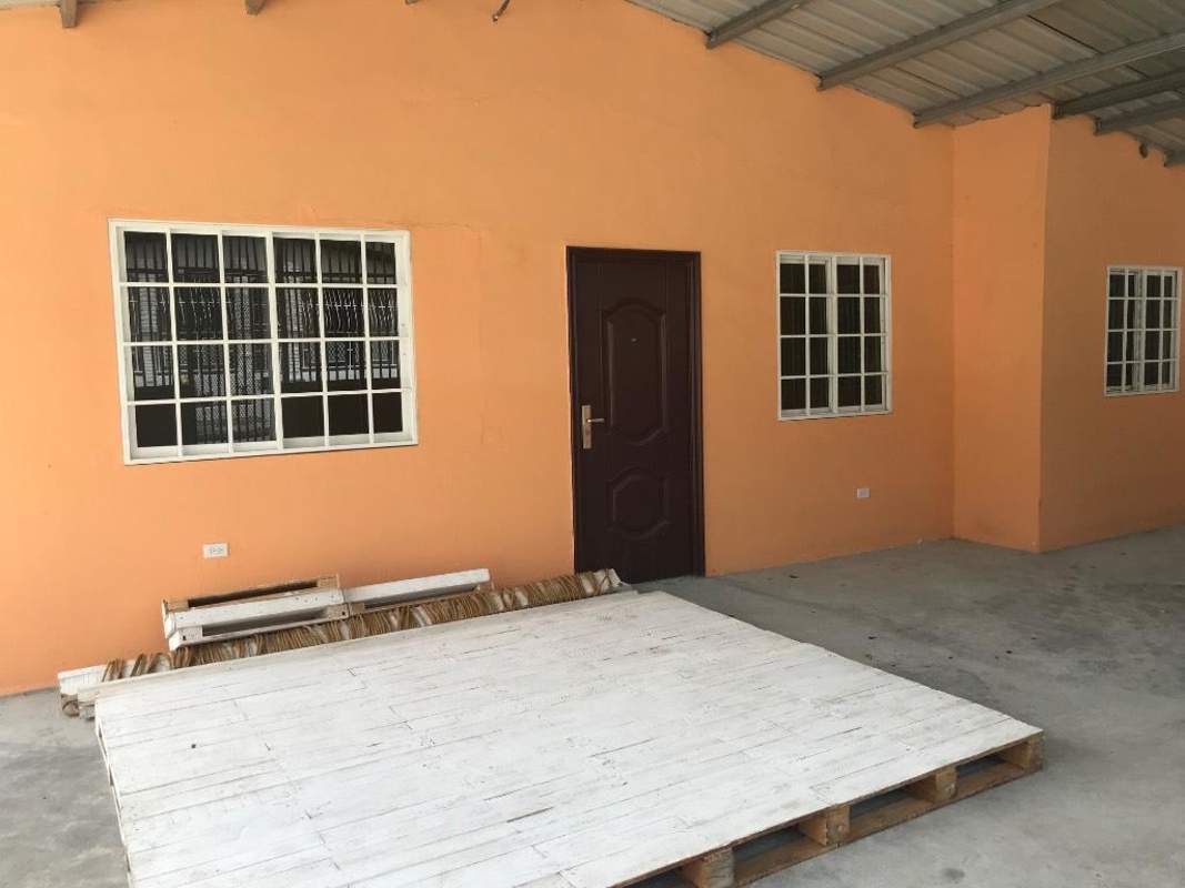 Exterior front view of orange-painted house with covered porch and barred windows in Pedregal Panama