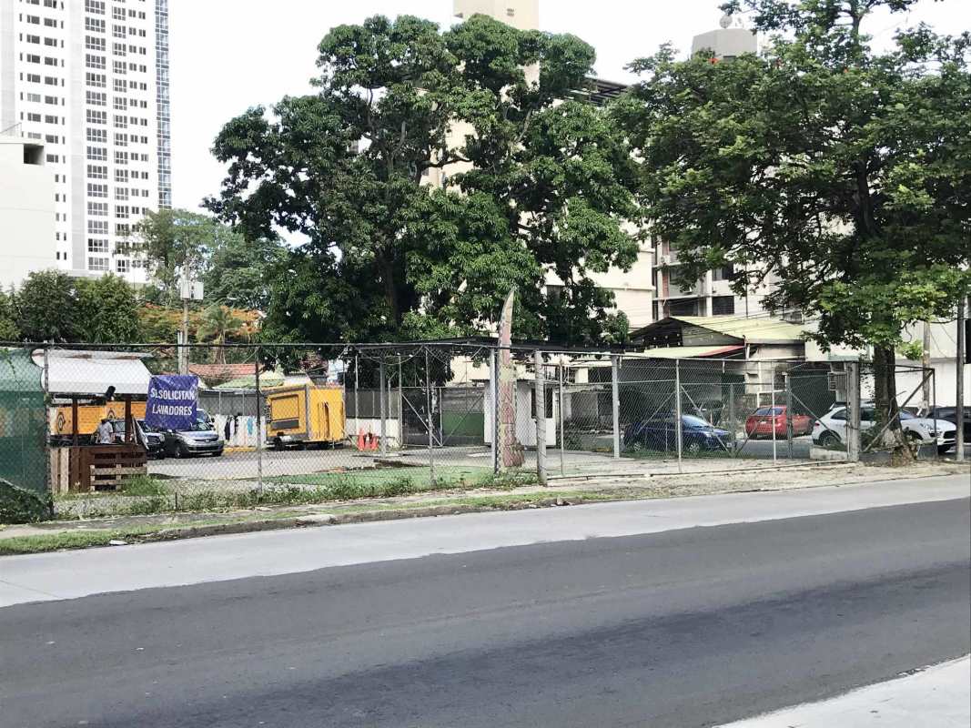 Busy urban street with corner fenced plot, mid-rise apartments, parked cars in Coco del Mar Panama City