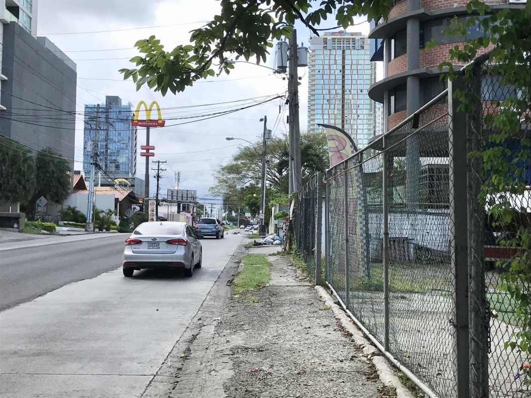 Urban street corner with sidewalk, mid-rise condos, signage, fenced vacant lot in Coco del Mar Panama