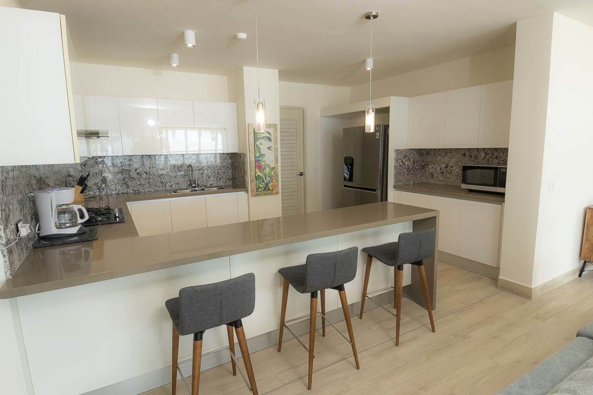 Coastal style kitchen with island, bar stools, marble backsplash, and stainless appliances in Punta Chame condo
