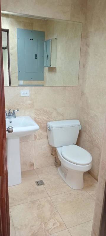 Compact modern bathroom with beige stone tiles, pedestal sink, large mirror in Panama World Trade Center Office