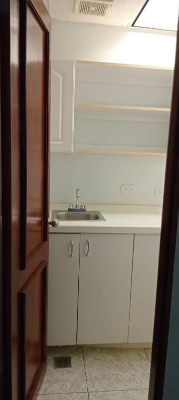 Small kitchenette with white cabinets, sink, open shelves inside Panama World Trade Center office in Marbella