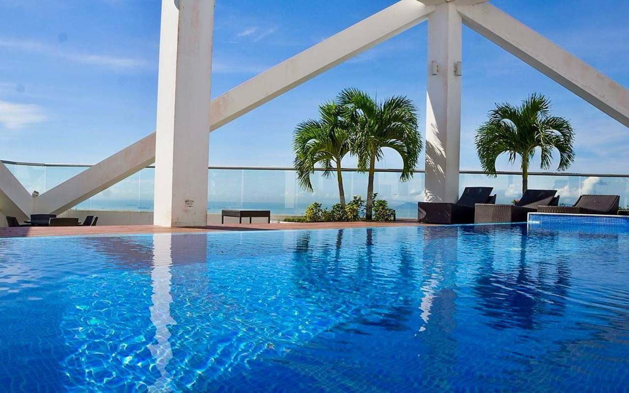 Panoramic oceanfront pool deck with infinity pool, lounge chairs and skyline backdrop