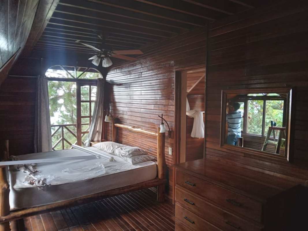 Wood-lined master bedroom with balcony access overlooking forest in mountain cabin Panama