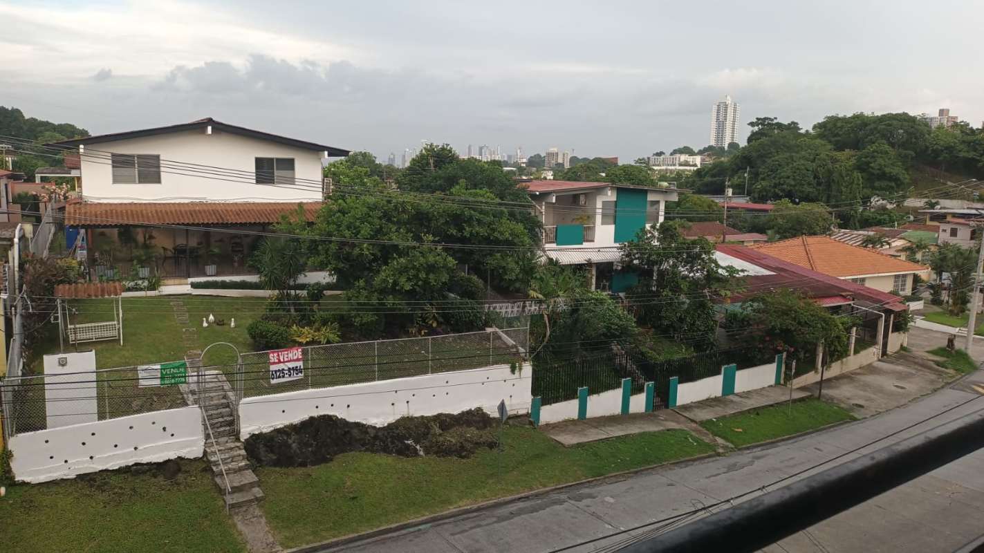 Residential neighborhood view with fenced houses, gardens, and skyline of Panama City