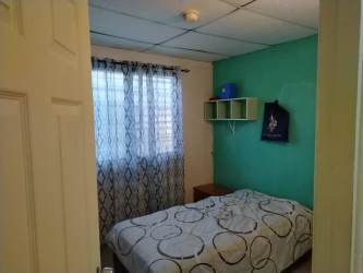 Bedroom with teal accent wall, bed, and window curtains in furnished house La Chorrera