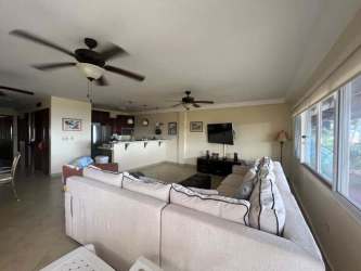 Open concept living room with sectional sofa, ceiling fans, big windows and connected kitchen in PH Malibu Beach