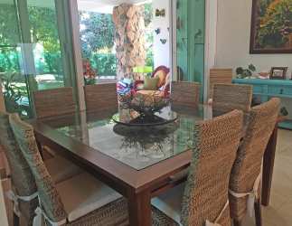 Coastal style dining with glass table, wicker chairs, turquoise cabinet near garden panorama in Punta Barco Village Panama