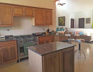 Contemporary kitchen with granite island, wood cabinets, stainless stove, open view to living space in Punta Barco Beach Home Panama