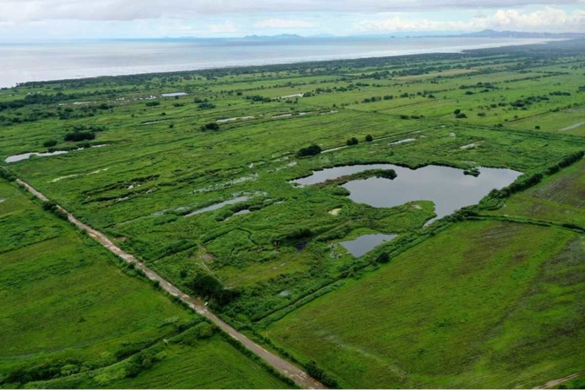 Wide aerial farmland with lakes, dirt roads and coastline in distance Pacora