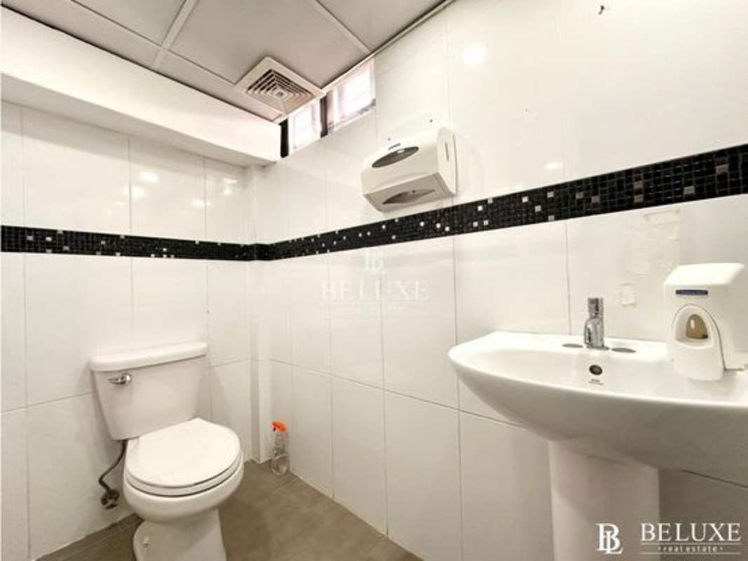 Restroom with white tiles, hygiene dispensers, and pedestal sink in commercial space Obarrio Panama