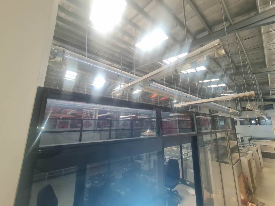 Modern mezzanine office area with glass partitions overlooking industrial warehouse floor in Panama City