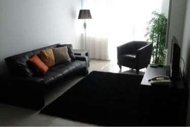 Modern living room with large window, blackout curtains, black sofa, bright natural light, and balcony overlooking Playa Corona