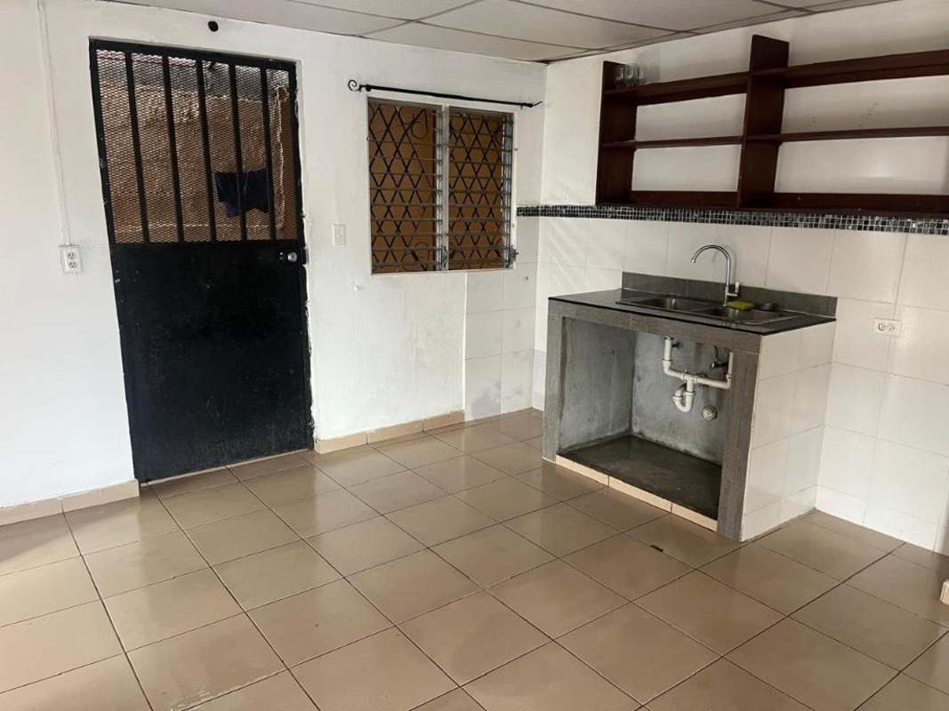 Simple kitchen with metal security door, barred window, sink and open shelving in Paraíso residence Panama