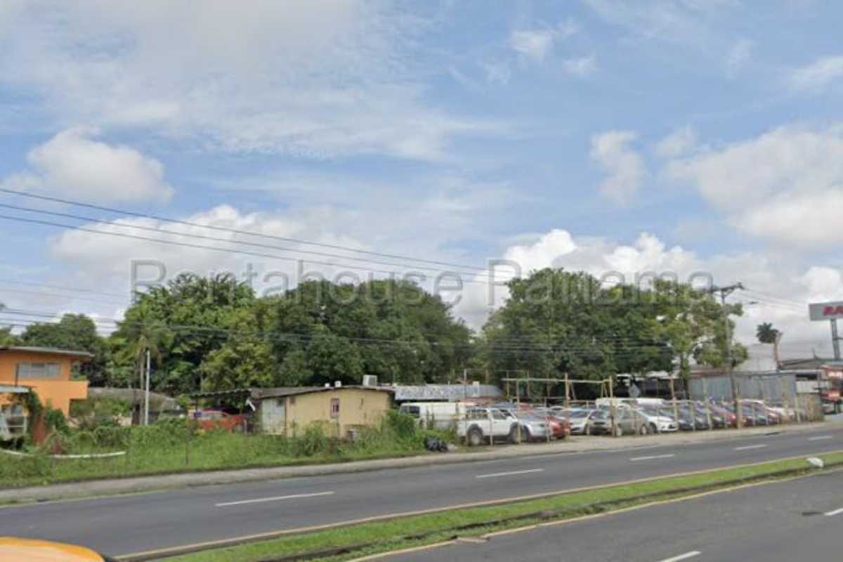 Roadside street view of fenced commercial property with parked cars and wide road frontage in Panama City
