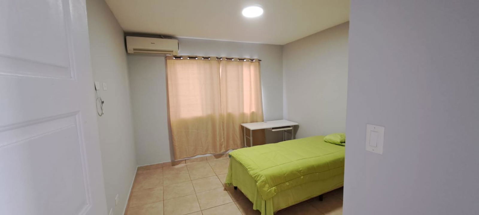 Bedroom setup with small desk, beige curtains, air conditioning split, minimalist décor in PH Alpes Paseo del Norte