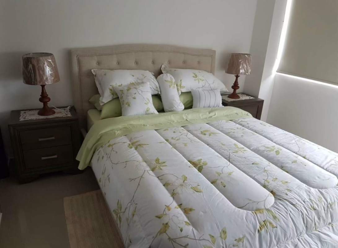 Cozy bedroom with floral bedding, tufted headboard and lamps at PH Sky Park Panama
