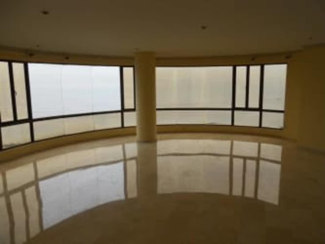 Bright living space with curved glass windows and marble floors overlooking the ocean