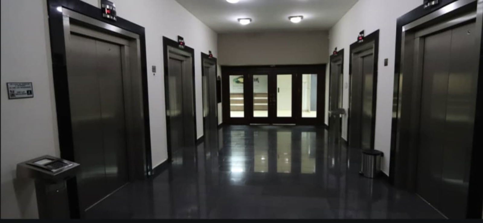 Modern elevator lobby with four elevators, glossy black flooring, bright lighting at Torre Banesco, Marbella Panama City