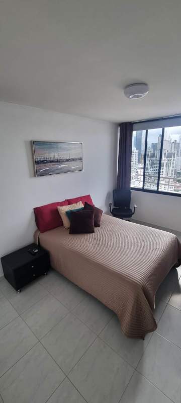 Furnished bedroom with wall-mounted TV, fan, large city-view window in PH Obarrio Tower Panama City