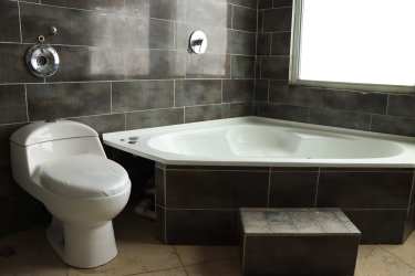 Bright bathroom with corner bathtub, dark tiles, frosted window in mountain house El Valle Panama
