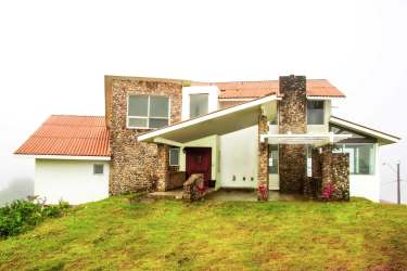Modern mountain house exterior with red-tiled roof, stone accents, large windows and landscaped gardens in El Valle