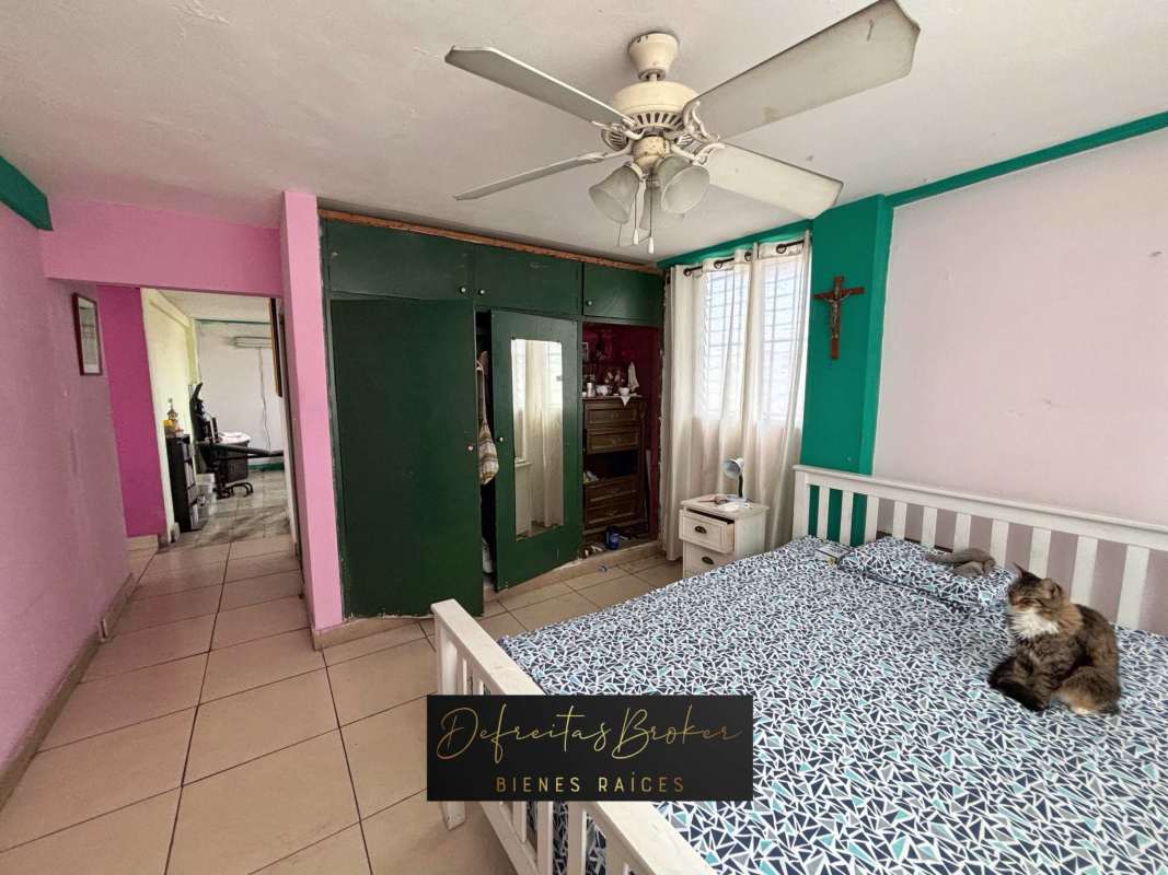 Bedroom with green wardrobe, white bed, ceiling fan, colorful walls in Parque Lefevre apartment Panama