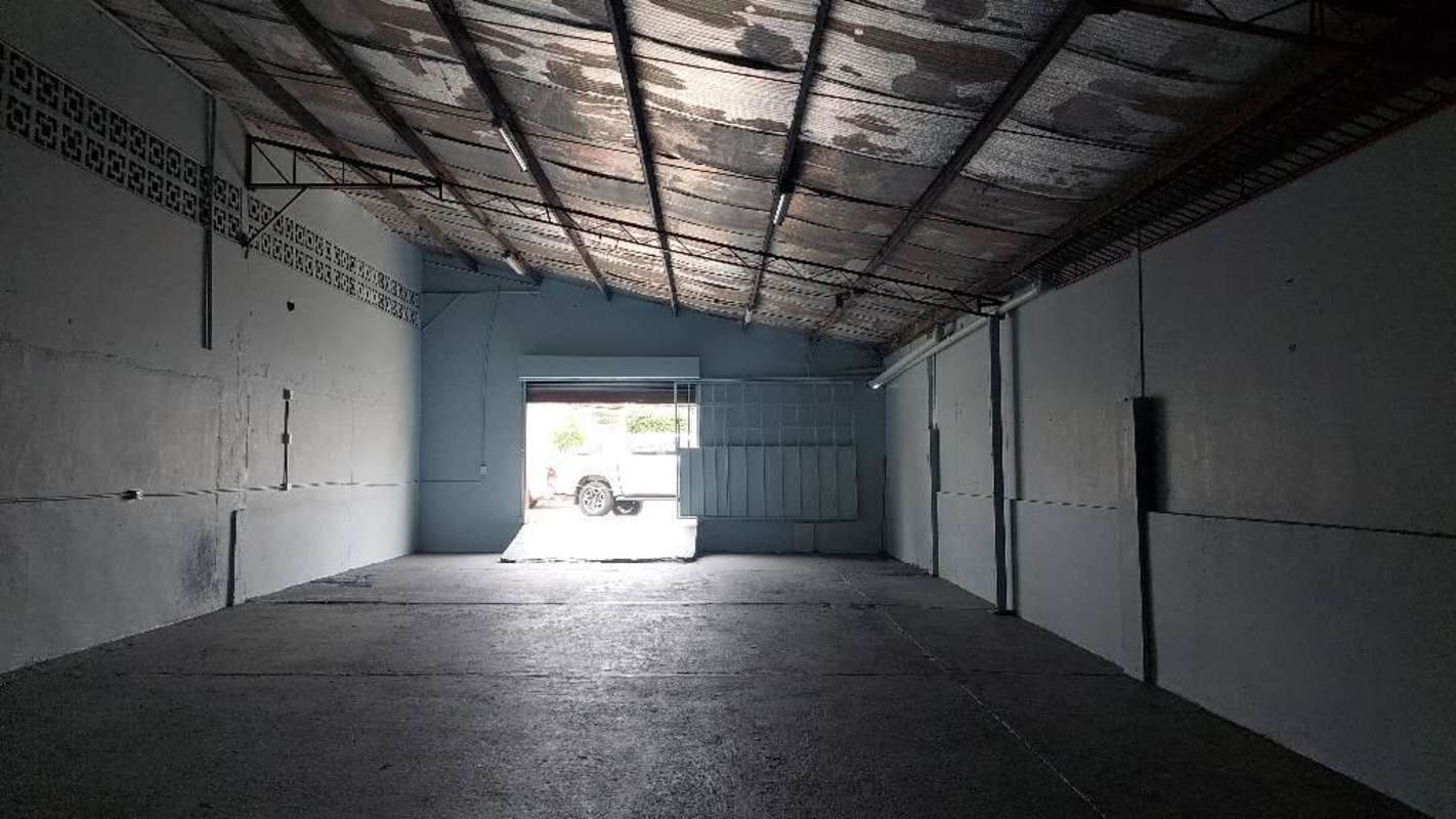 Interior view of warehouse with metal roll-up door partially open and vehicle outside in Miraflores Panama