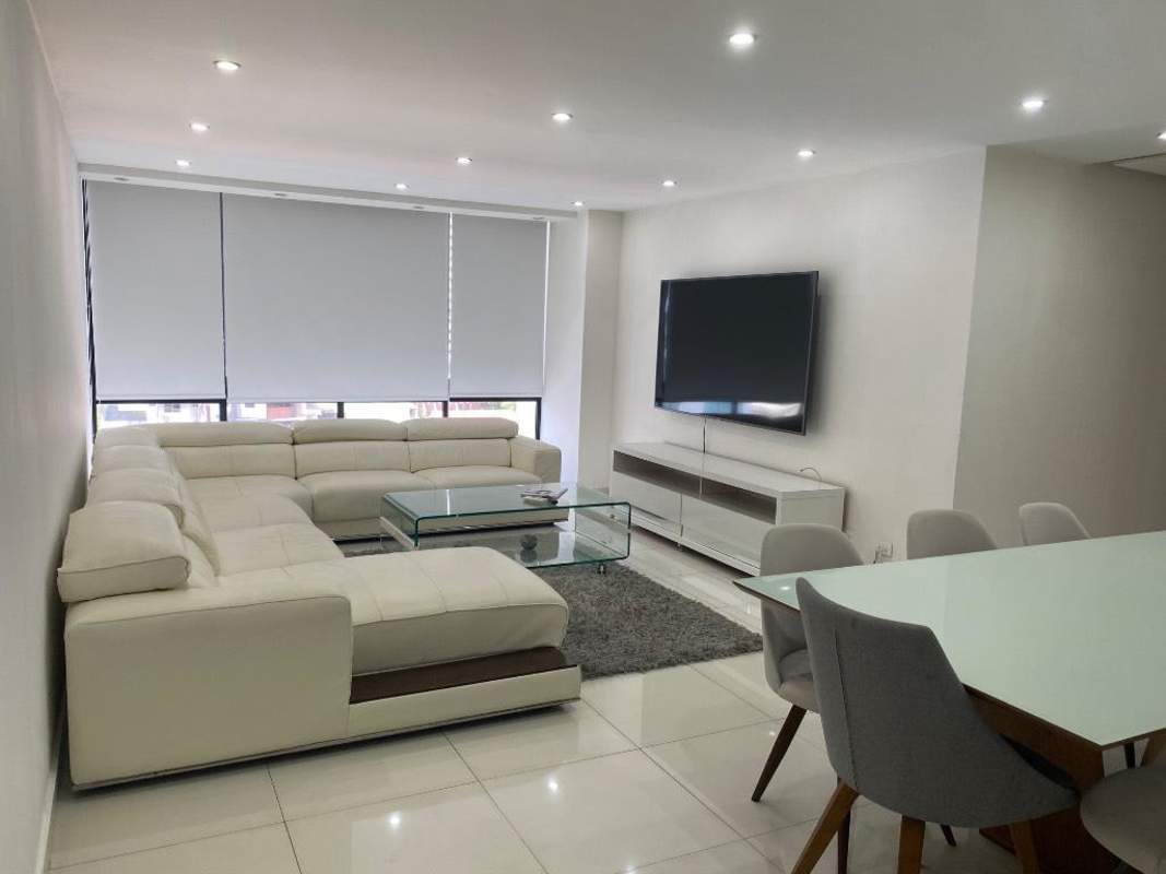 Spacious living room with sectional sofa, glass dining table, mounted TV, and minimalist decor in PH Torres Coco Mar San Francisco Panama