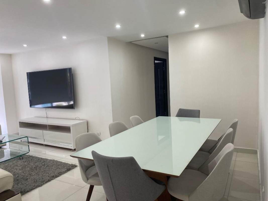 Modern dining space with glass table, gray chairs, wall-mounted TV in apartment at PH Torres Coco Mar Panama City