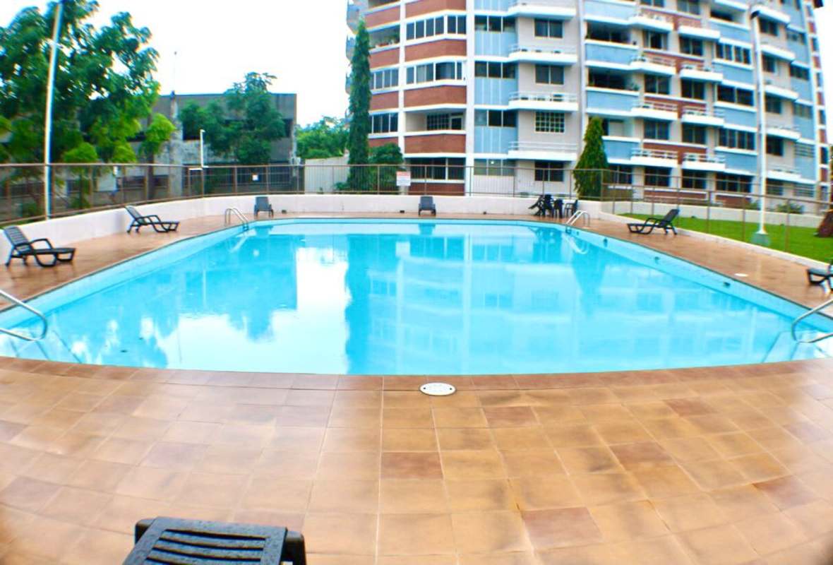Outdoor swimming pool with lounge chairs and apartment building at Llano Bonito Gardens Panama City