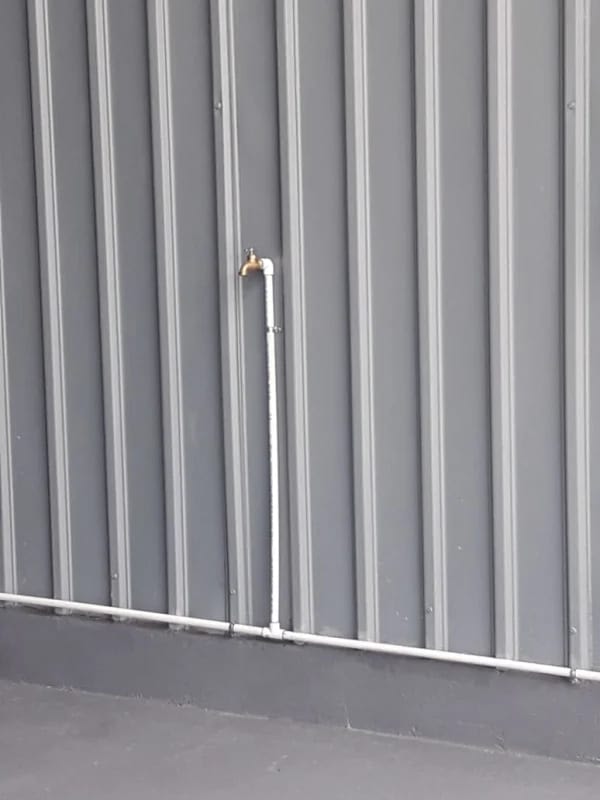 Exterior wall with bronze faucet mounted on pipe attached to corrugated metal siding at Diablo warehouse