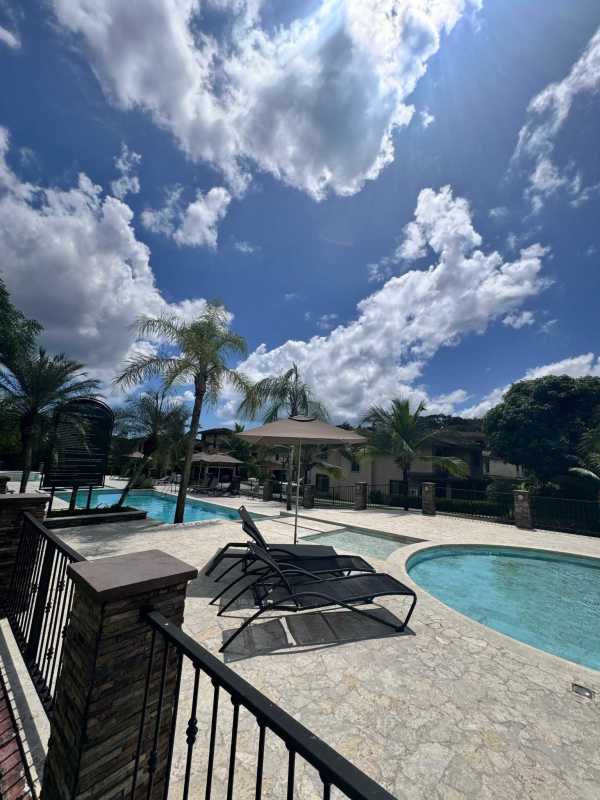 Outdoor swimming pool surrounded by palm trees and lounge chairs in Embassy Club Clayton