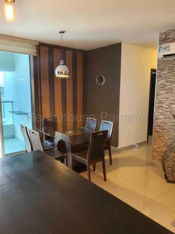 Open plan dining and kitchen with glass table, pendant light, wood cabinets PH Diamond Tower San Francisco Panama