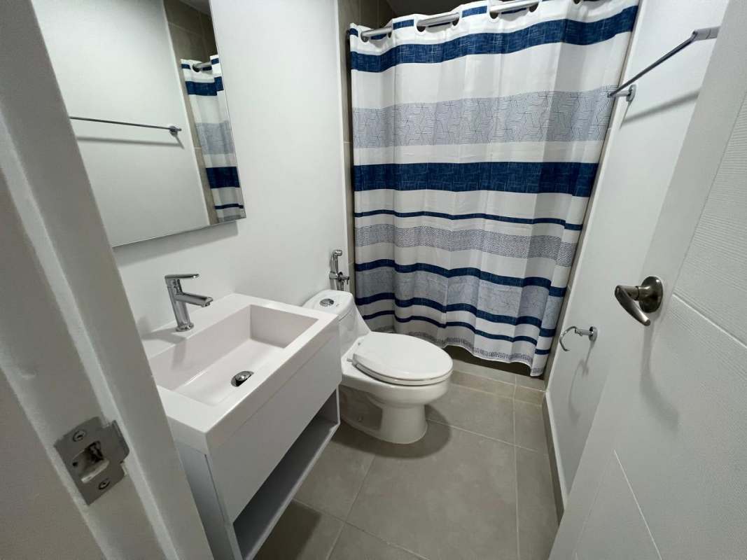 Bright bathroom with blue shower curtain modern sink mirror at Panama Viejo Residences for rent