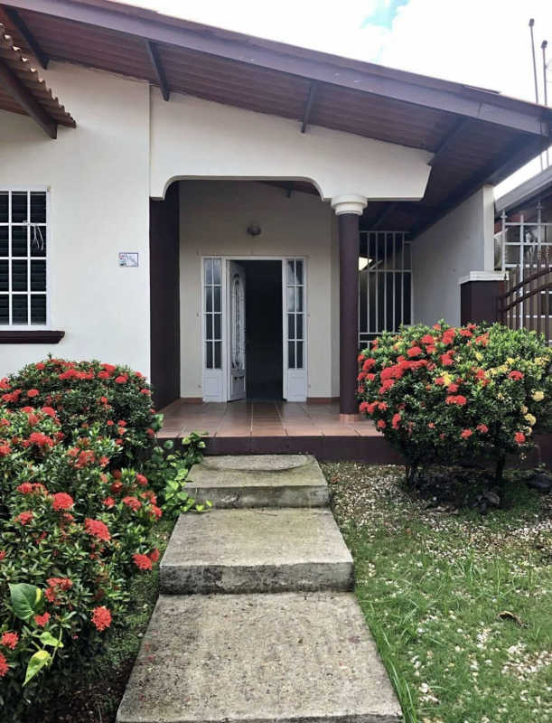 Traditional single-story house with tiled porch, garden path, green shrubs in Terrazas de Brisas del Golf Panama City