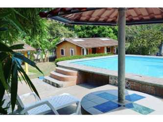 Raised outdoor swimming pool with patio furniture, green lawn and garden in Playa Corona hostel complex Panama
