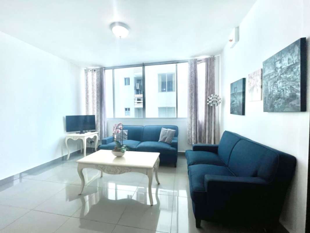 Bright living room with blue sofas, TV console and large window at PH Quartier San Francisco Panama