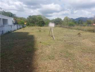Open green vacant land bordered by fence and adjacent houses in Malibú beach community Panama
