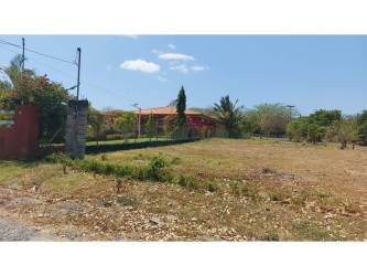 Fenced open lot with tropical landscaping and red rooftop house Coronado Panama