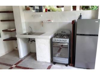 Compact indoor kitchen with gas stove, refrigerator, stainless sink at Playa Blanca inn