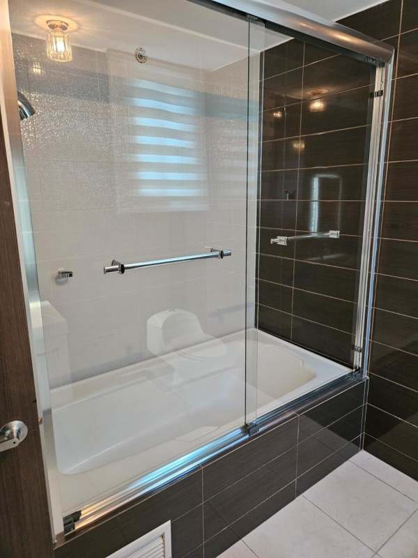 Bathroom with bathtub, glass shower doors, dark tile wall and window PH Midtown Panama City
