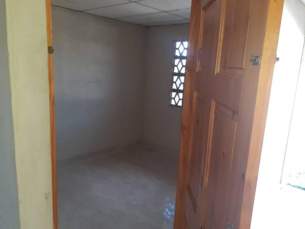 Small bedroom with light gray walls, ceramic tile, drop ceiling, and wooden door in Chepo Panama