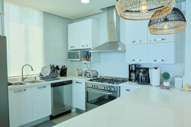 Open contemporary kitchen in beachfront condo PH Rio Mar with white counters appliances