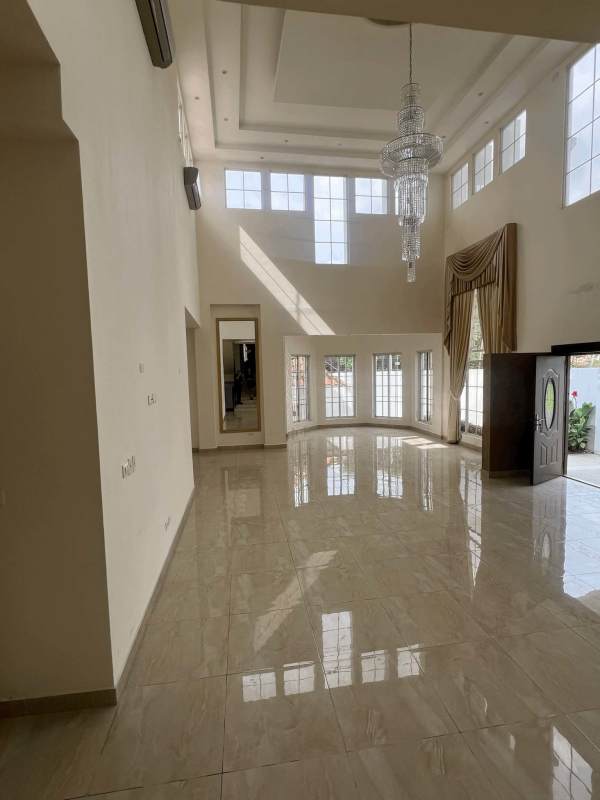 Spacious double-height living room with large windows, marble floors, and chandelier in luxury house Altos del Golf Panama