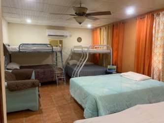 Bedroom with peach walls, twin beds, ceiling fan and large curtained windows in Playa Malibu beach house Panama