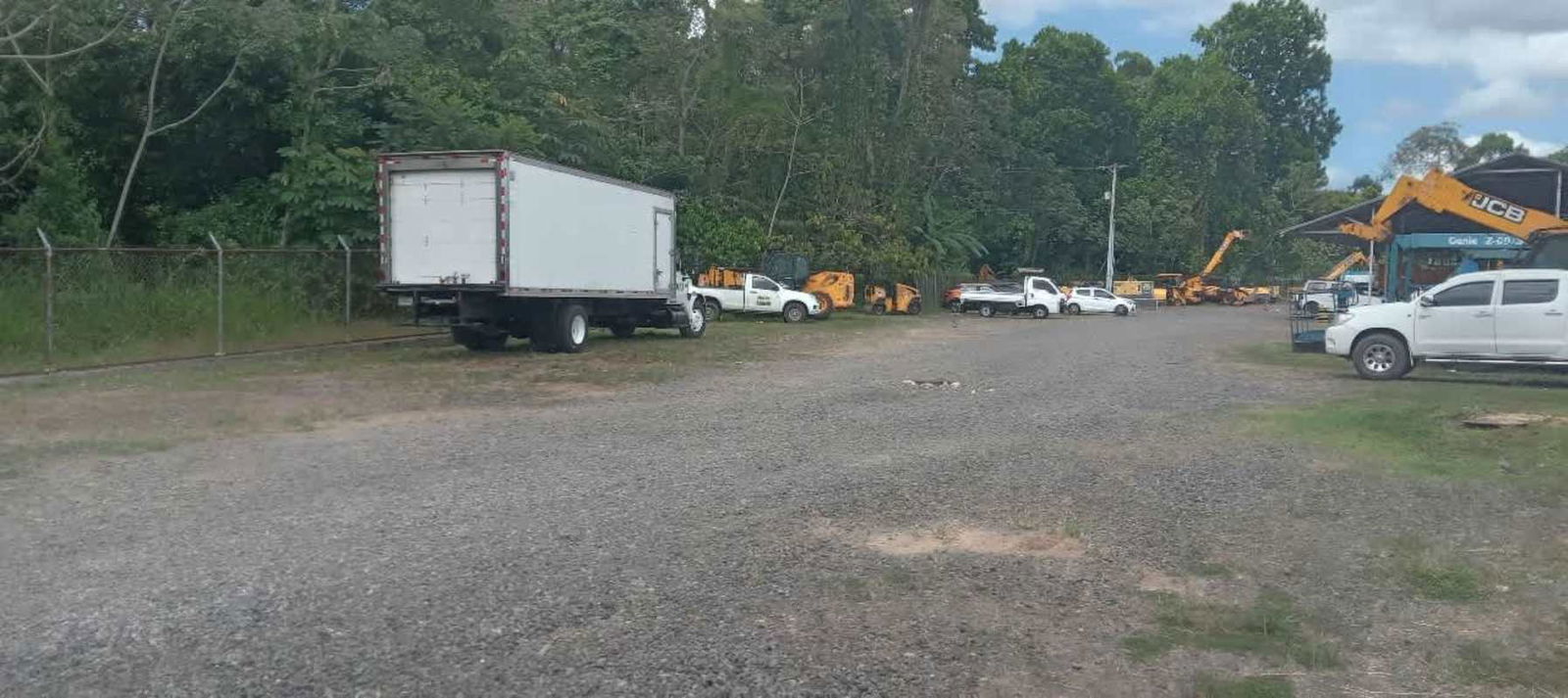 Wide gravel lot with parked trucks equipment near dense greenery at commercial plot in Panama City