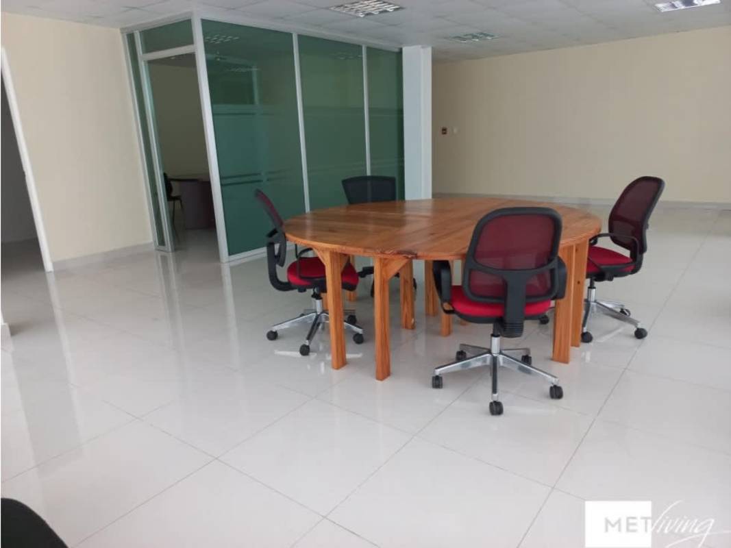 Compact meeting room with round wooden table and four black chairs, tiled floor, drop ceiling, in modern Bella Vista office Panama