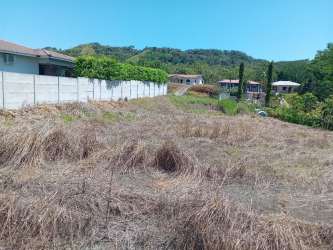 Lot bordered with wall, dry grass terrain, neighbor houses and hills background in David Panama
